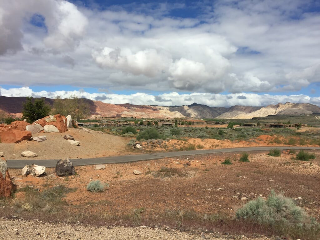 Narrow road in the middle of desert with mountains and big clouds