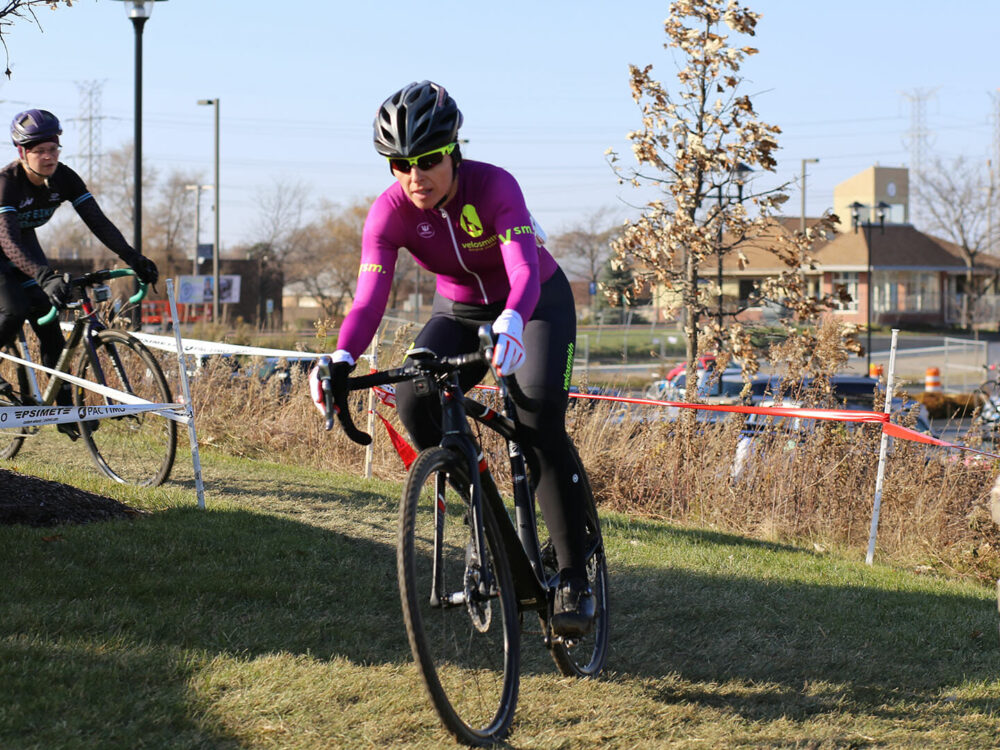 Theia Friestedt racing cyclocross down hill on grass on Trek Boone with another racer behind
